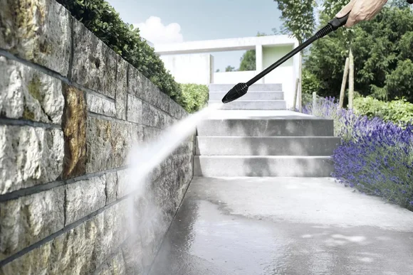 Person reinigt Steinmauer mit Hochdruckreiniger